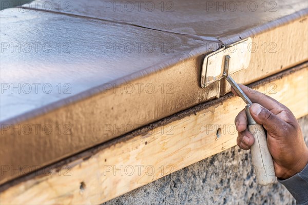 Construction worker using hand groover on wet cement forming coping around new pool