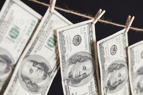Hundred dollar bills hanging from a clothesline on a dark background