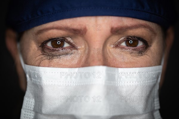 Tearful stressed female doctor or nurse wearing medical face mask on dark background