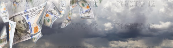 Several 100 dollar bills falling from stormy cloudy sky banner