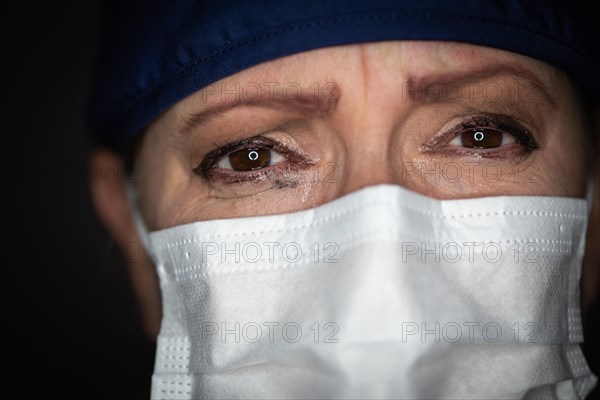 Tearful stressed female doctor or nurse wearing medical face mask on dark background