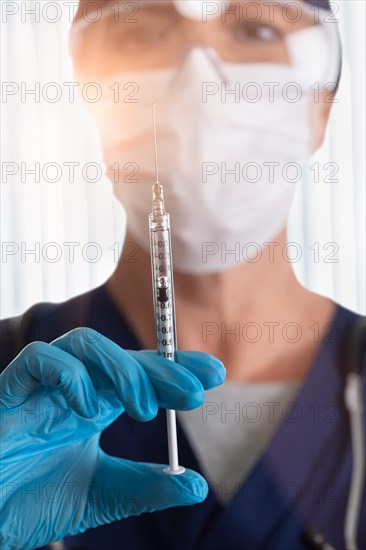 Doctor or nurse wearing medical face mask and goggles holding syringe filled with medicine