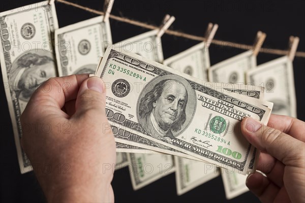 Male hands holding hundred dollar bills with several hanging from a clothesline on a dark background