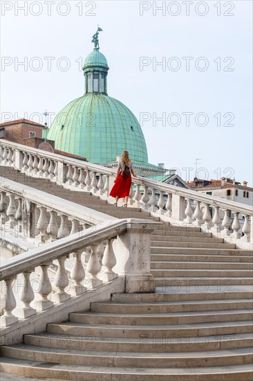 Young woman with red skirt walks over a bridge at the Grand Canal