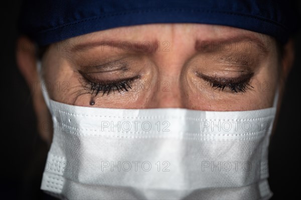 Tearful stressed female doctor or nurse wearing medical face mask on dark background