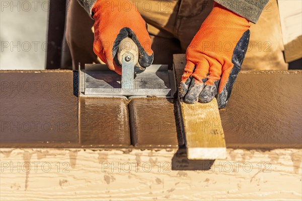 Construction worker using hand groover on wet cement forming coping around new pool