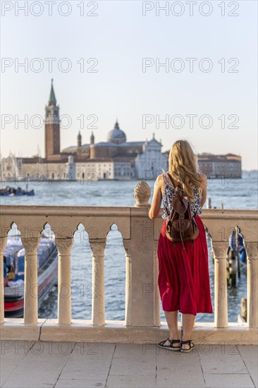 Young woman tourist sitting by the sea looking at the church Chiesa di San Giorgio Maggiore