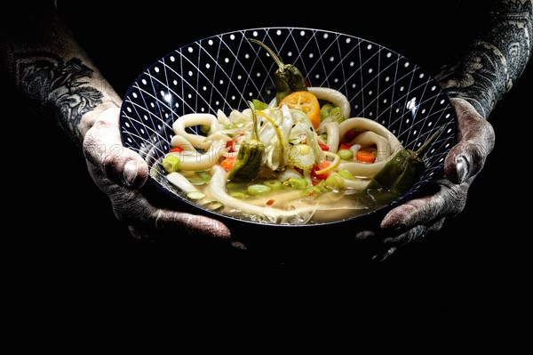 Tattooed hands hold plate with udon bowl