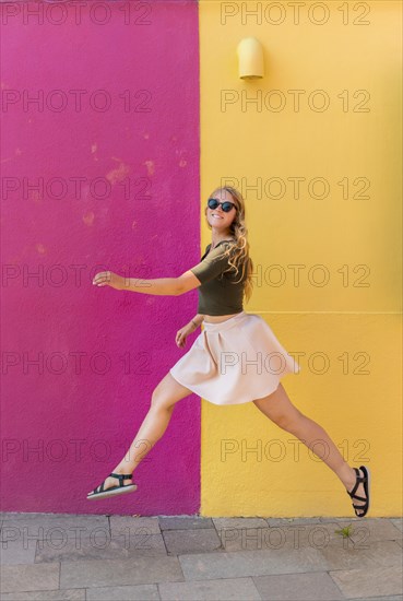 Young woman in dress jumps happily in front of colorful house