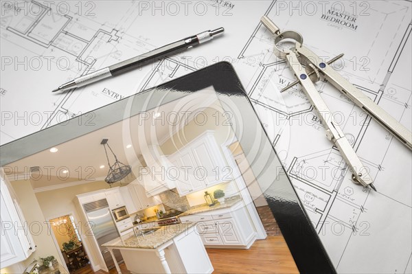 Computer tablet showing finished kitchen sitting on house plans with pencil and compass