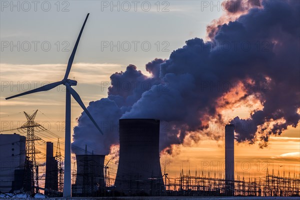 Wind turbine in front of steaming coal-fired power plant at sunset