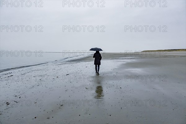 Woman with umbrella walking on the beach in rainy weather