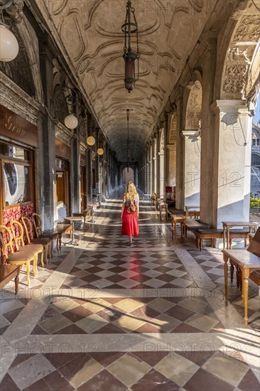 Young woman tourist walking under arcades at St. Mark's Square