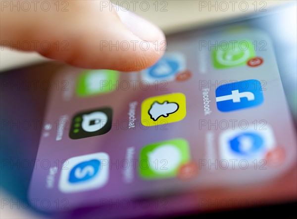 Finger tapping on screen with app icons of messenger services and social networks