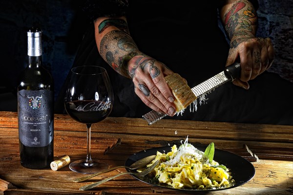 Woman with tattooed hands grates parmesan on fresh pasta