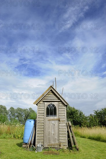 Small wooden garden shed with tools outside and plastic water butt