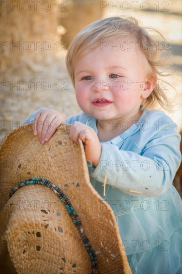 Adorable baby girl with cowboy hat in a country rustic setting at the pumpkin patch