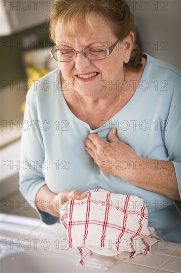 Grimacing senior adult woman at kitchen sink with chest pains