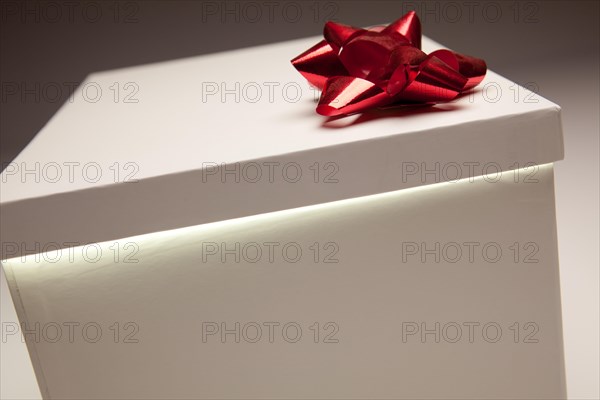 Gift box with red bow lid revealing very bright contents on a gradated background