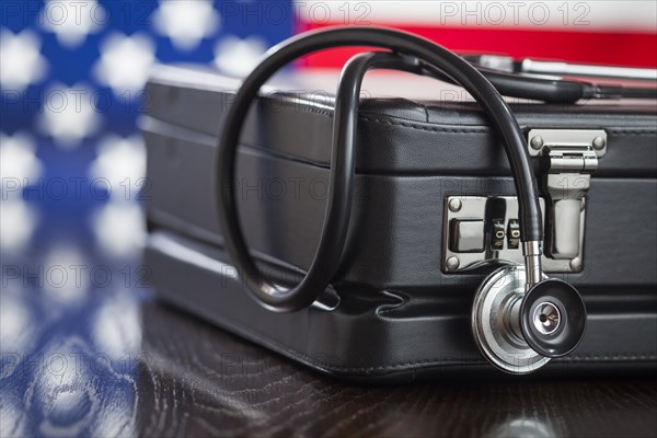 Leather briefcase and stethoscope resting on table with american flag behind