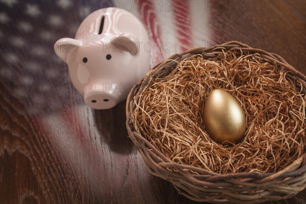 Golden egg in nest and piggy bank with american flag reflection on wooden table