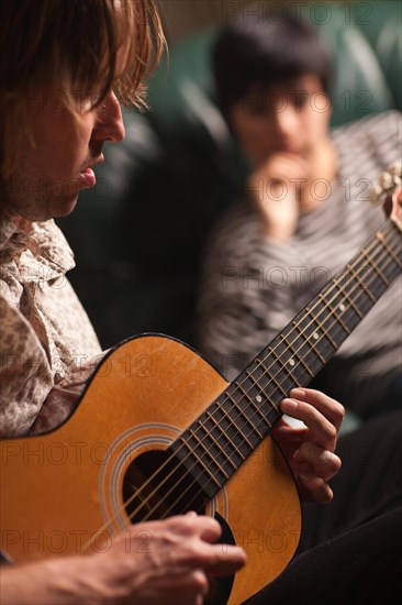 Young musician plays his acoustic guitar as friend in the background listens