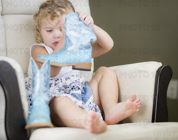 Adorable blonde haired blue eyed little girl putting on cowboy boots