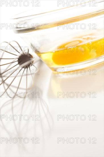 Hand mixer with eggs in a glass bowl on a reflective white background