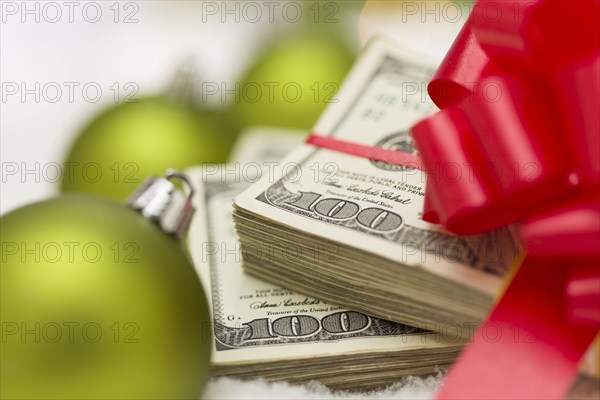 Stack of one hundred dollar bills with red bow near green christmas ornaments on snow flakes