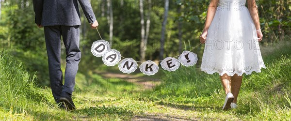 Bride and groom holding garland with THANKS on forest path