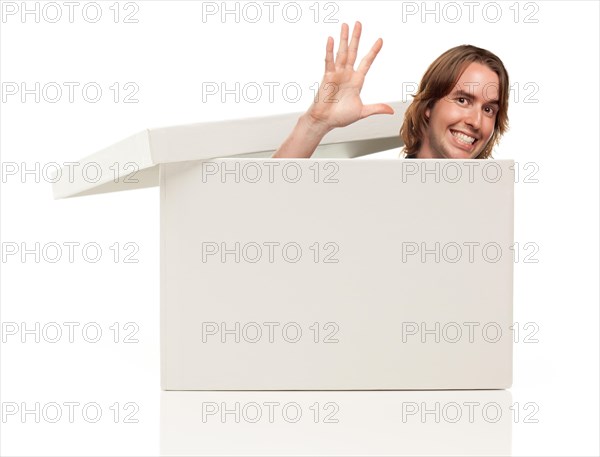 Young man waving his hand and popping his head from a blank white box isolated on a white background