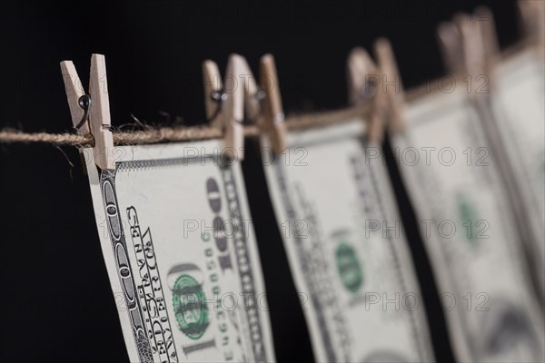 Hundred dollar bills hanging from a clothesline on a dark background