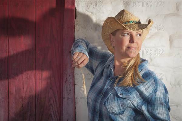 Beautiful cowgirl wearing cowboy hat leaning against old adobe wall and red door