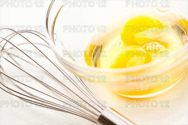 Hand mixer with eggs in a glass bowl on a reflective white background