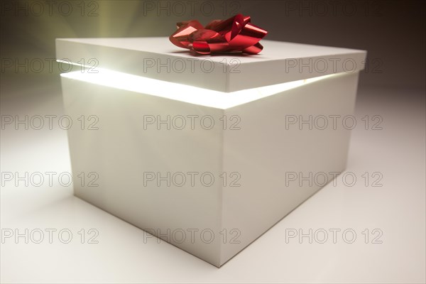 Gift box with red bow lid revealing very bright contents on a gradated background