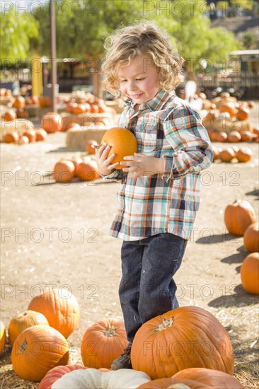 Adorable little boy sitting and holding his pumpkin in a rustic ranch setting at the pumpkin patch