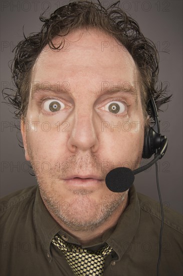 Stunned businessman wearing phone headset against a grey background