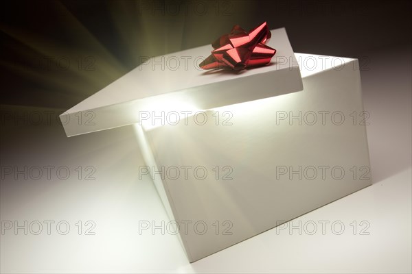 Gift box with red bow lid revealing very bright contents on a gradated background