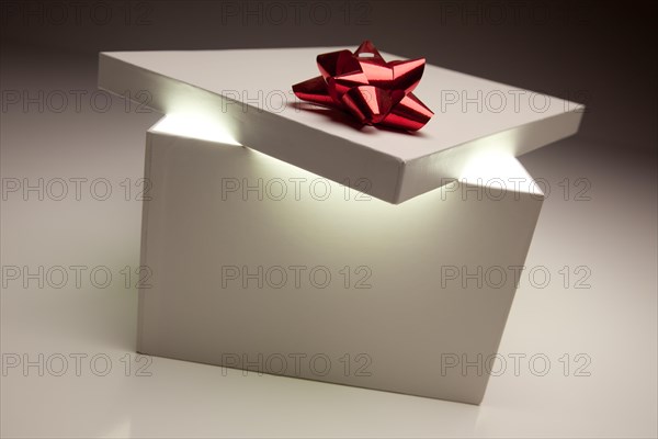 Gift box with red bow lid revealing very bright contents on a gradated background