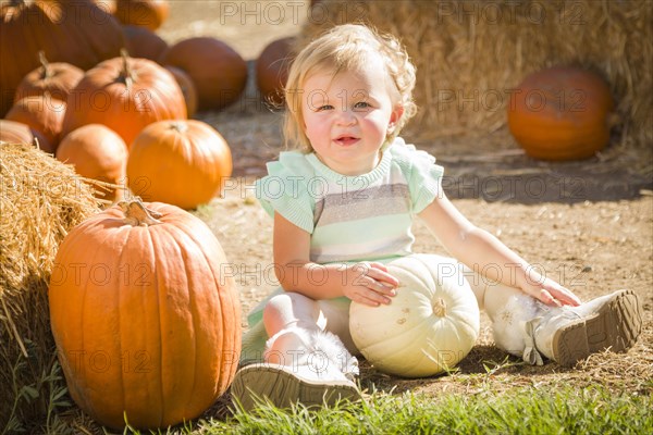 Adorable baby girl holding a pumpkin in a rustic ranch setting at the pumpkin patch