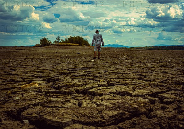Man standing at cracked earth at the bottom dried up lake