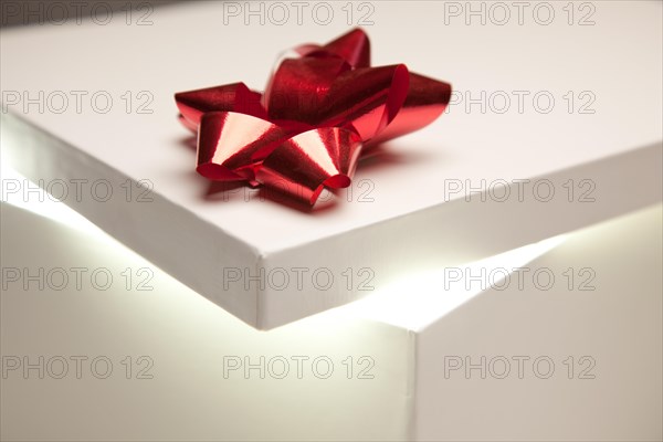 Gift box with red bow lid revealing very bright contents on a gradated background