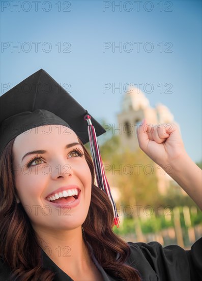 Happy graduating mixed-race woman in black cap and gown celebrating on campus