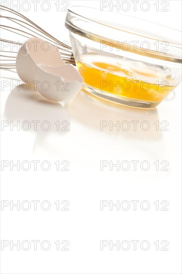 Hand mixer with eggs in a glass bowl on a reflective white background
