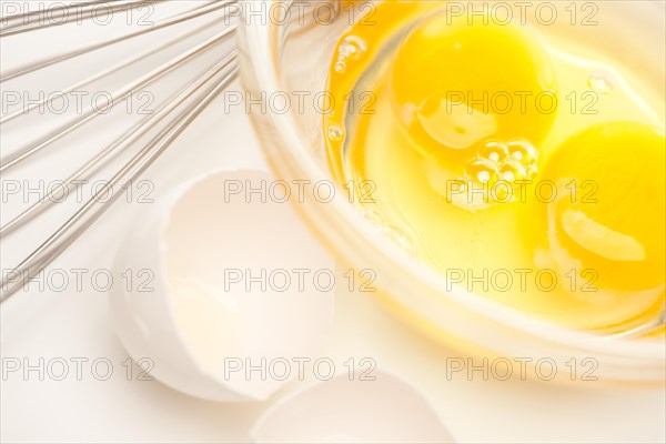 Hand mixer with eggs in a glass bowl on a reflective white background
