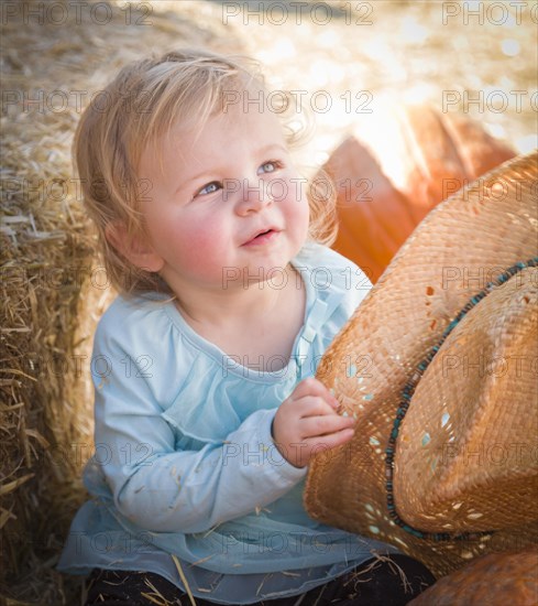 Adorable baby girl with cowboy hat in a country rustic setting at the pumpkin patch