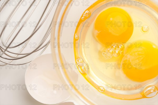 Hand mixer with eggs in a glass bowl on a reflective white background