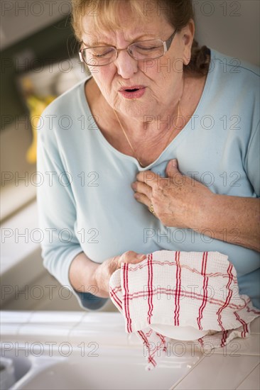 Grimacing senior adult woman at kitchen sink with chest pains