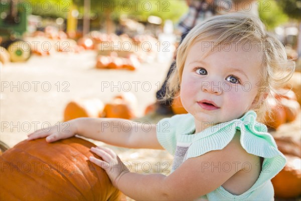 Adorable baby girl having fun in a rustic ranch setting at the pumpkin patch