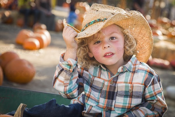 Adorable little boy wearing cowboy hat at pumpkin patch farm